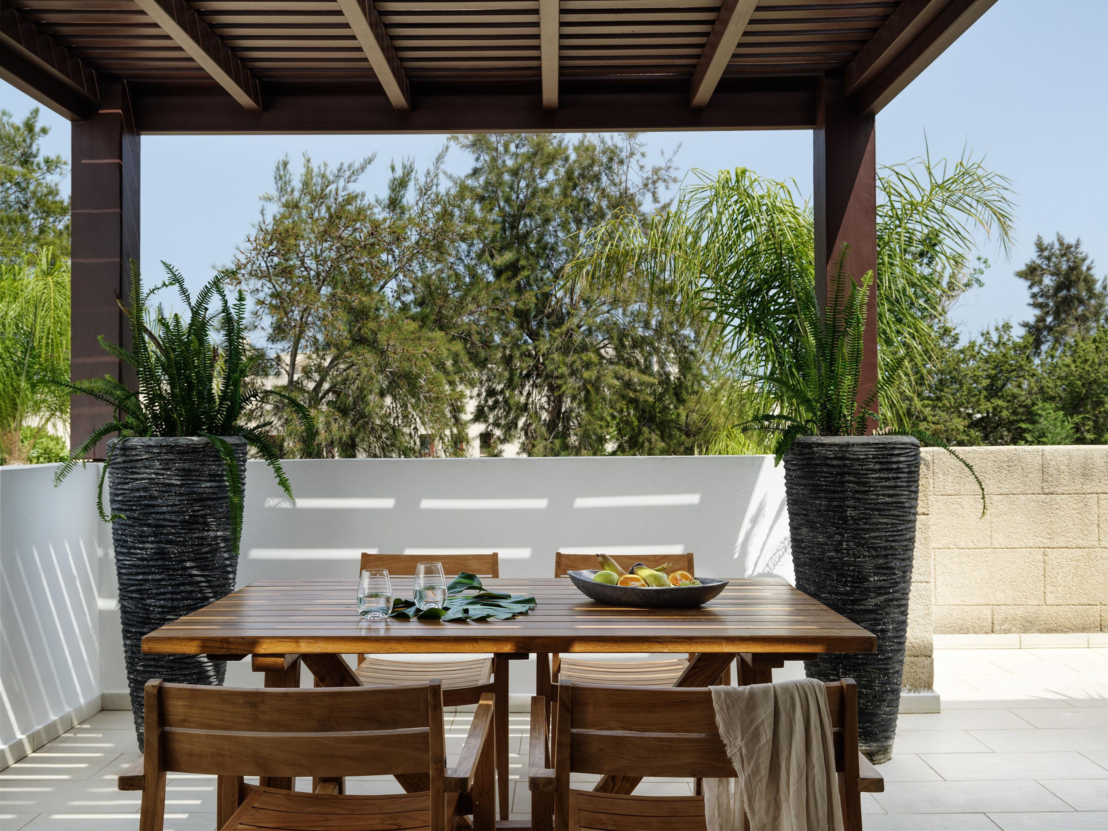 Un patio al aire libre con una mesa de madera, sillas y plantas en macetas.