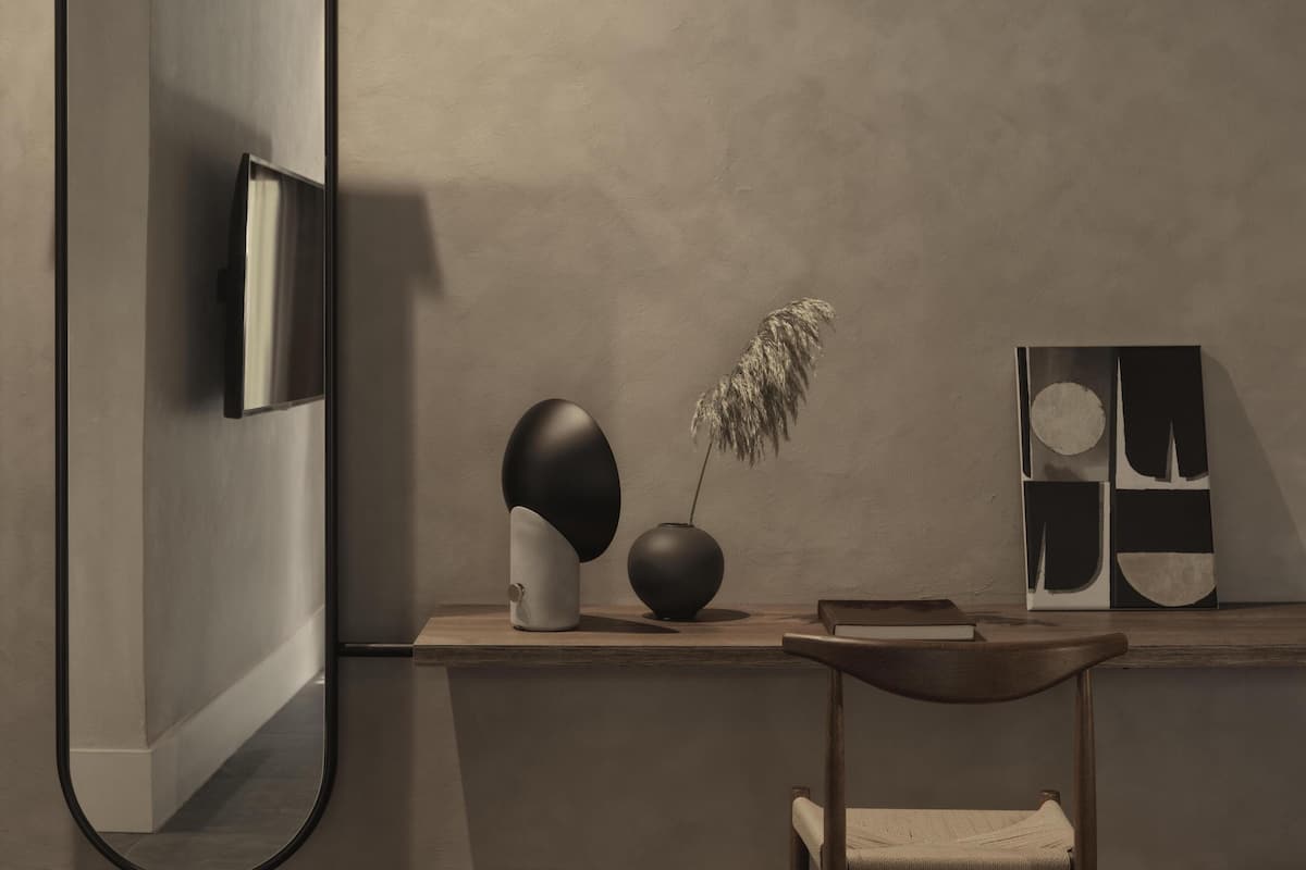 Un interior moderno con diseño minimalista, que incluye un televisor de pantalla plana montado en la pared, un escritorio de madera con un jarrón de plumas de grama de pampa seca, y una silla.