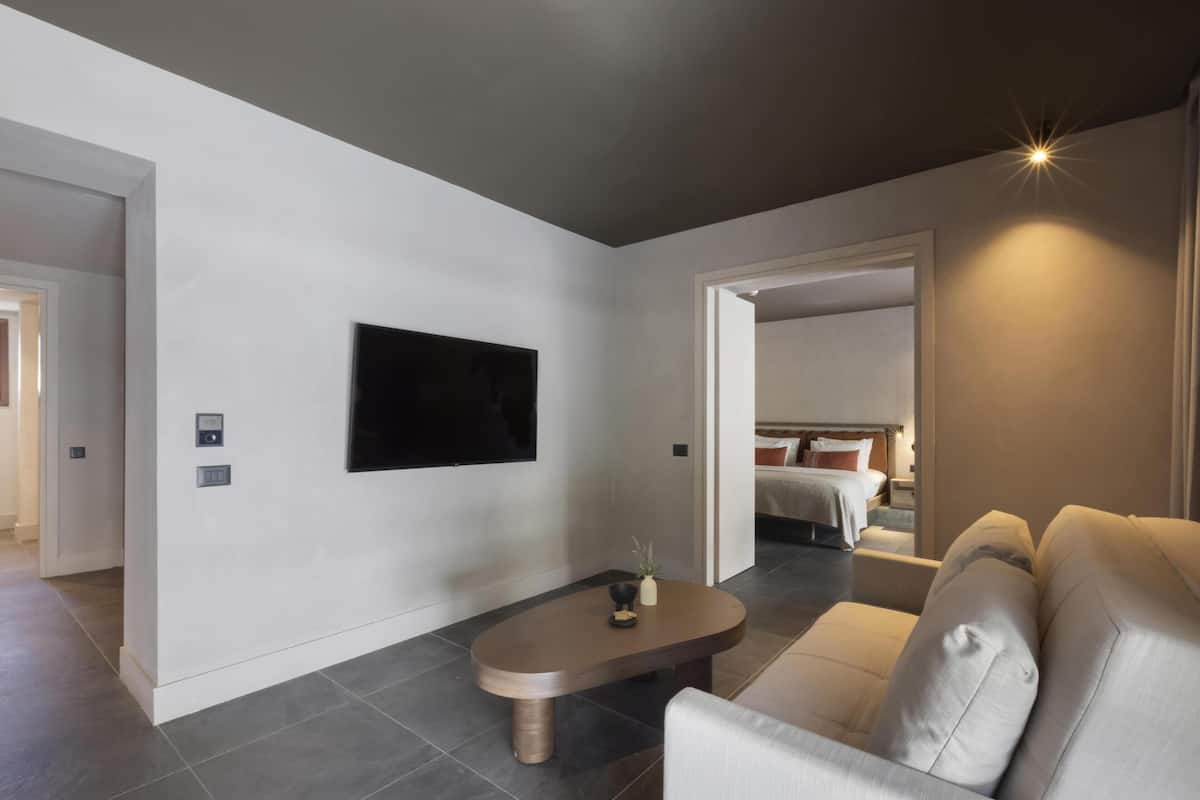 Una sala de estar moderna con un televisor de pantalla plana montado en la pared, un sofá, una mesa de centro y una puerta que da a un dormitorio.