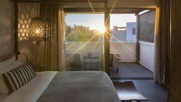 A hotel room with a bed, a hanging light fixture, a balcony with a table and chairs, and a view of the outside.