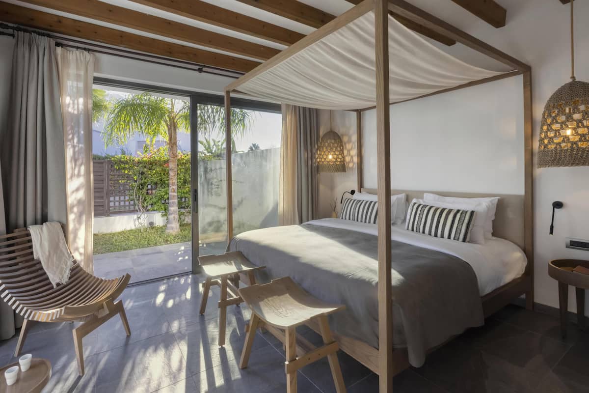 Un dormitorio con cama con dosel, sillas de madera, una mesita y vistas al exterior.
