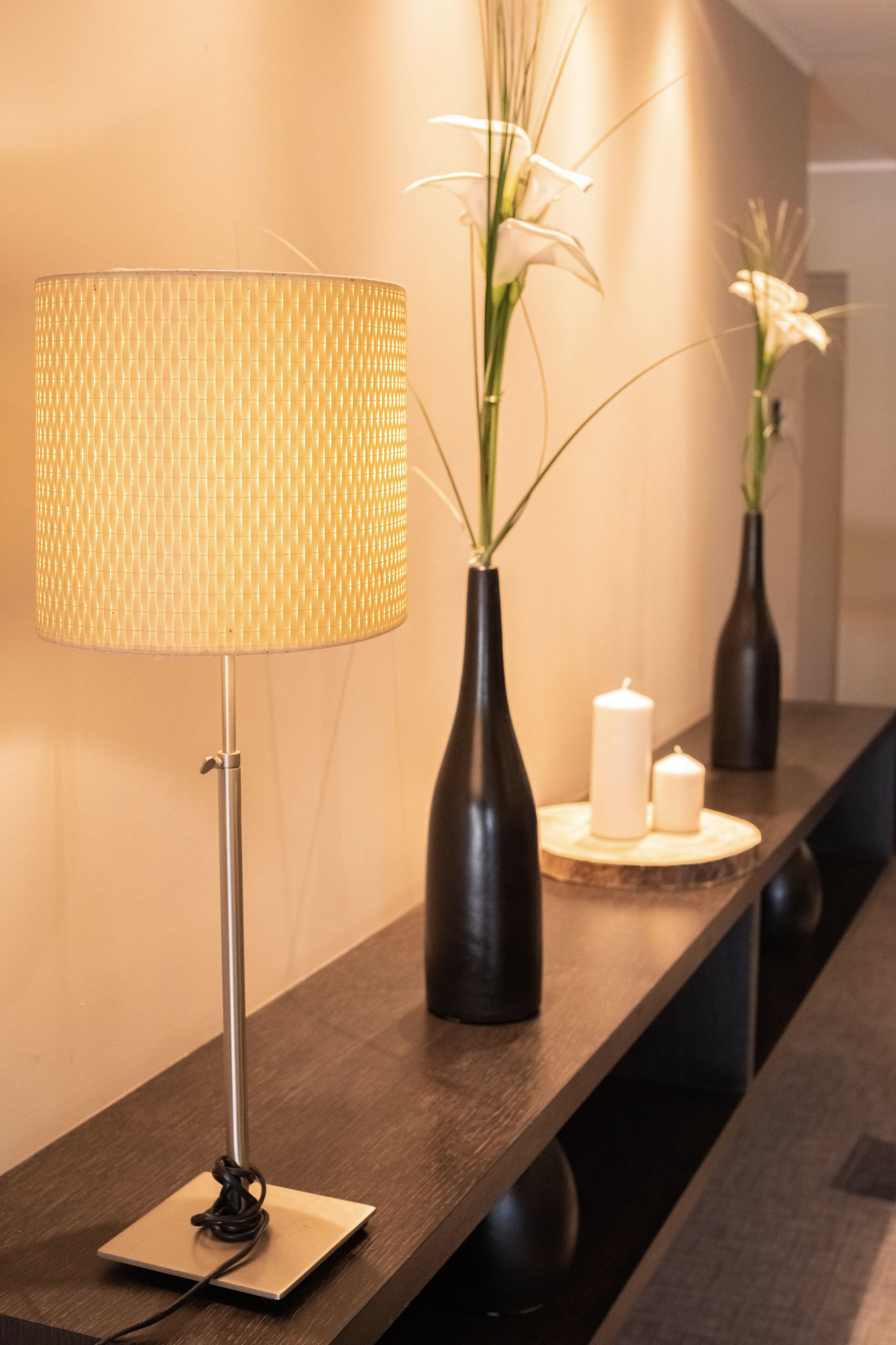A modern hotel reception area with a floor lamp, vases with flowers, and candles on a wooden console table.