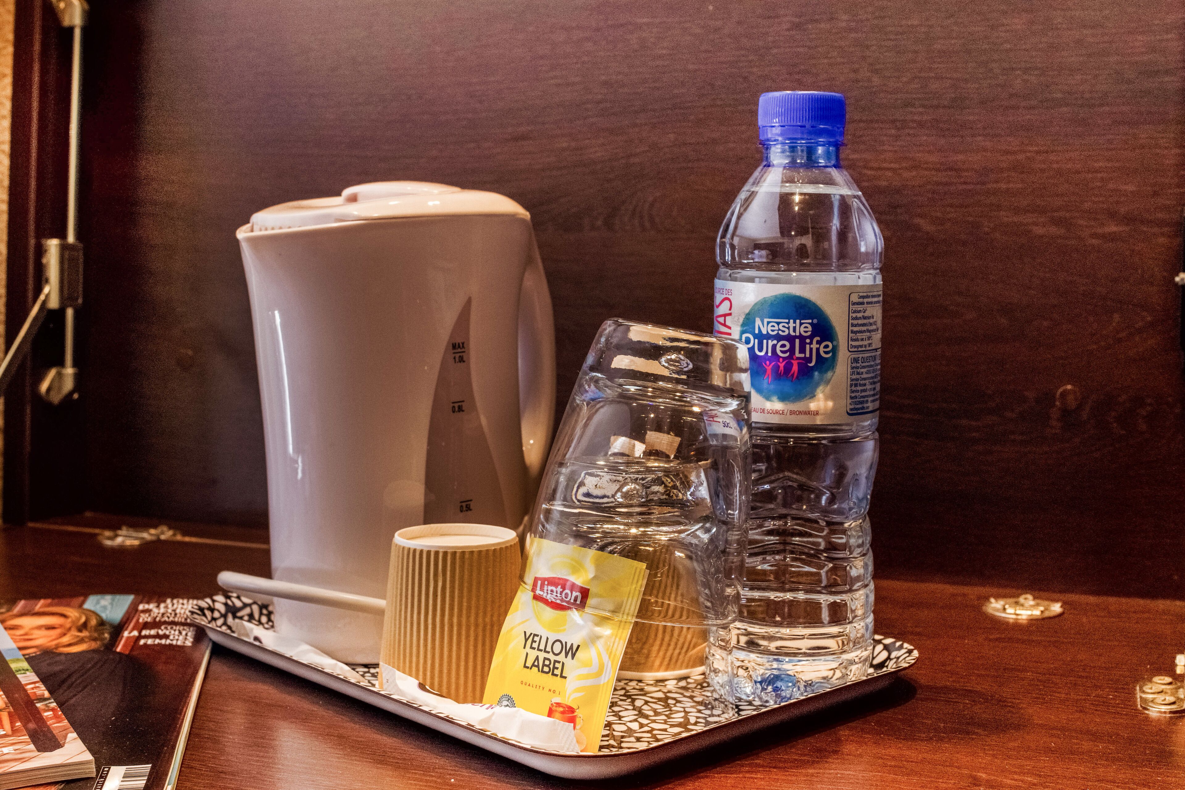 A tray with a coffee maker, a bottle of Nestle Pure Life water, a glass, and a yellow Lipton tea bag.
