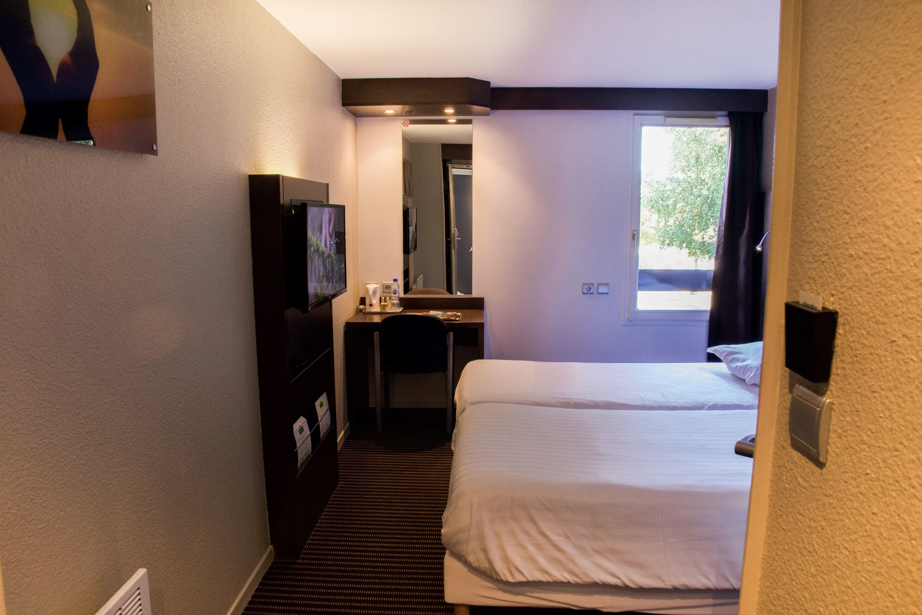 Hotellihuone, jossa on sänky, työpöytä, peili ja televisio.