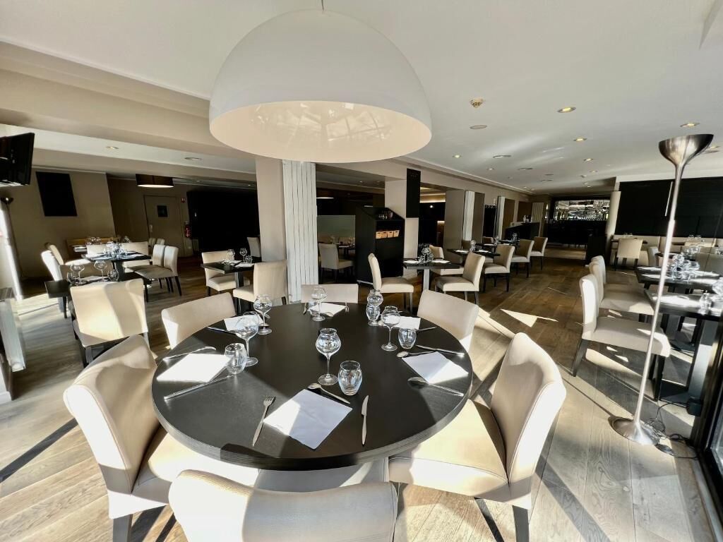 Un comedor moderno con mesas redondas, sillas blancas y una lámpara central grande.