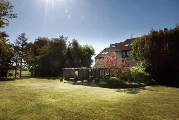 A spacious outdoor area with a covered seating area, surrounded by trees and a house in the background. - Parc Hotel (Carvin)