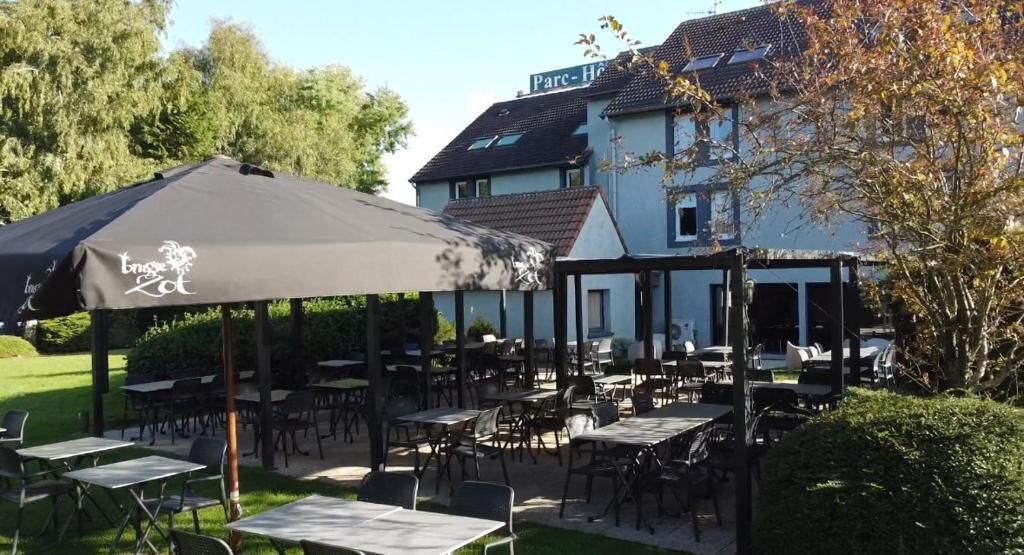 An outdoor seating area with tables and chairs, a covered umbrella, and a building in the background.