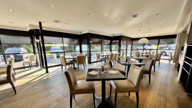 Een modern restaurantinterieur met houten vloeren, ronde tafels en beige stoelen.