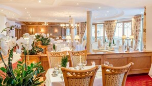 A formal dining room with tables set for service, elegant chandeliers, and large windows with curtains. - Austria Bellevue (Soelden)