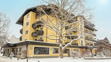 Ein mehrstöckiges Hotel mit gelber Fassade, Balkonen und verschneiter Landschaft.