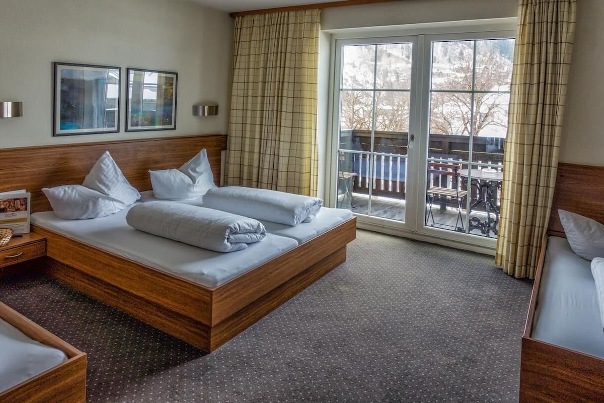 Een hotelkamer met een groot bed, een houten hoofdeinde, een klein nachtkastje en uitzicht op het omliggende landschap via een schuifdeur.