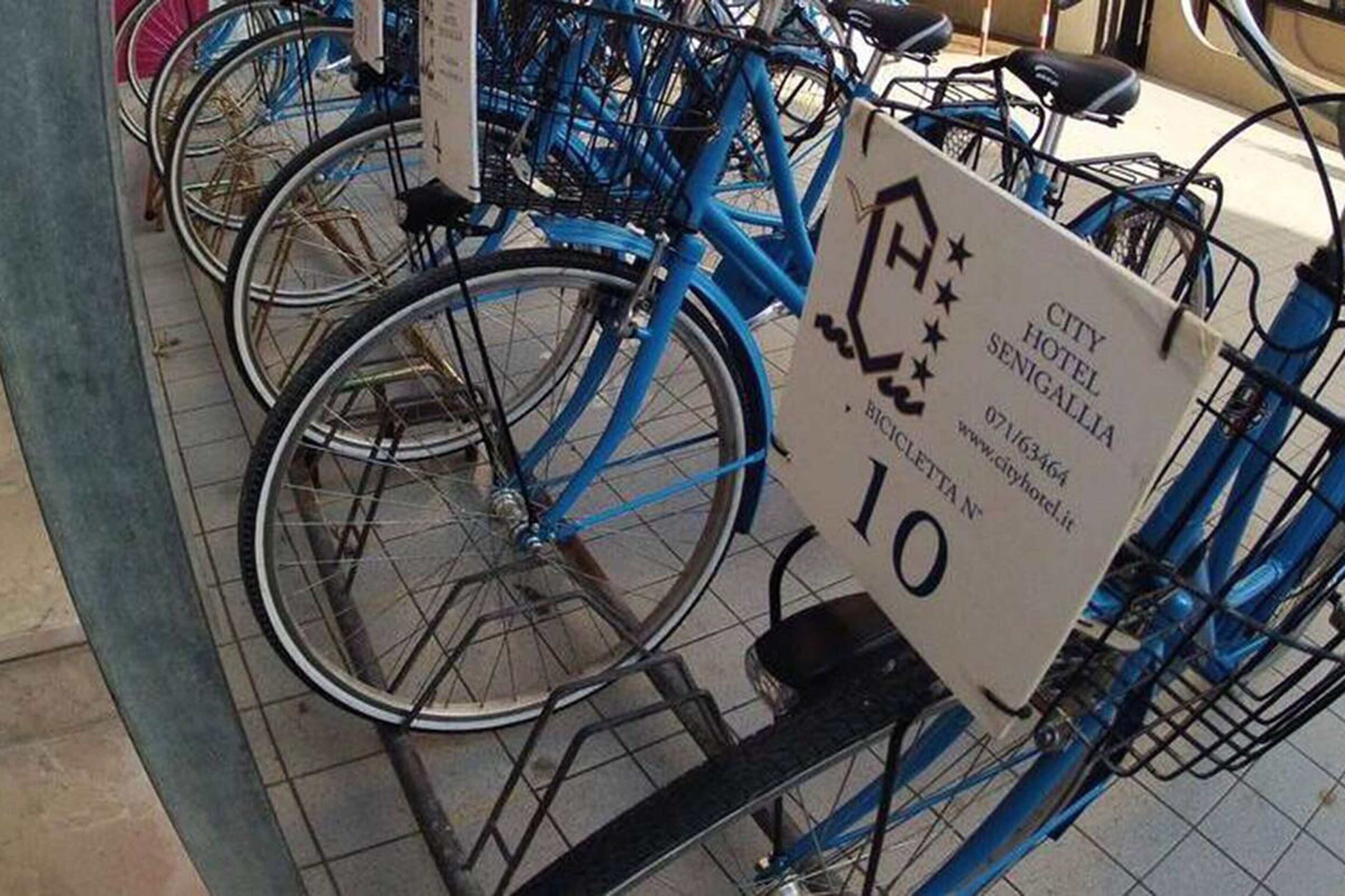 A row of blue bicycles parked in a designated area with a sign indicating the City Hotel Senigallia.