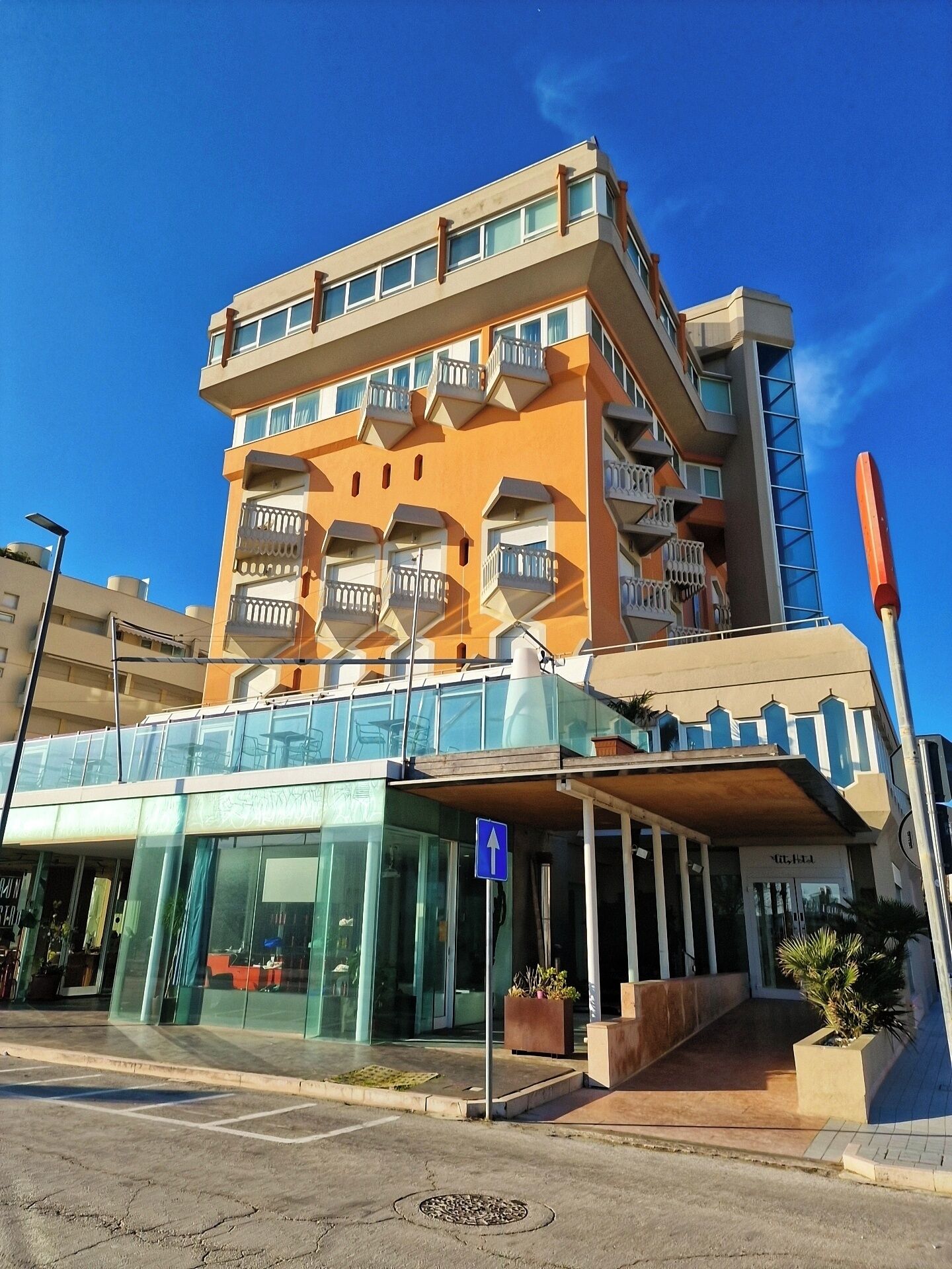 Un hôtel à plusieurs étages, doté de balcons, d’une entrée en verre et d’une enseigne bleue indiquant la direction.