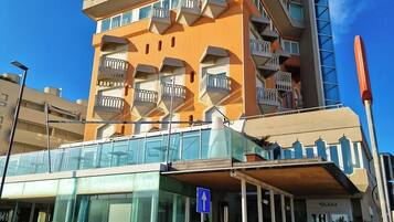 Ein mehrstöckiges Hotel mit Balkonen, einem Glastürbereich und einem blauen Hinweisschild.