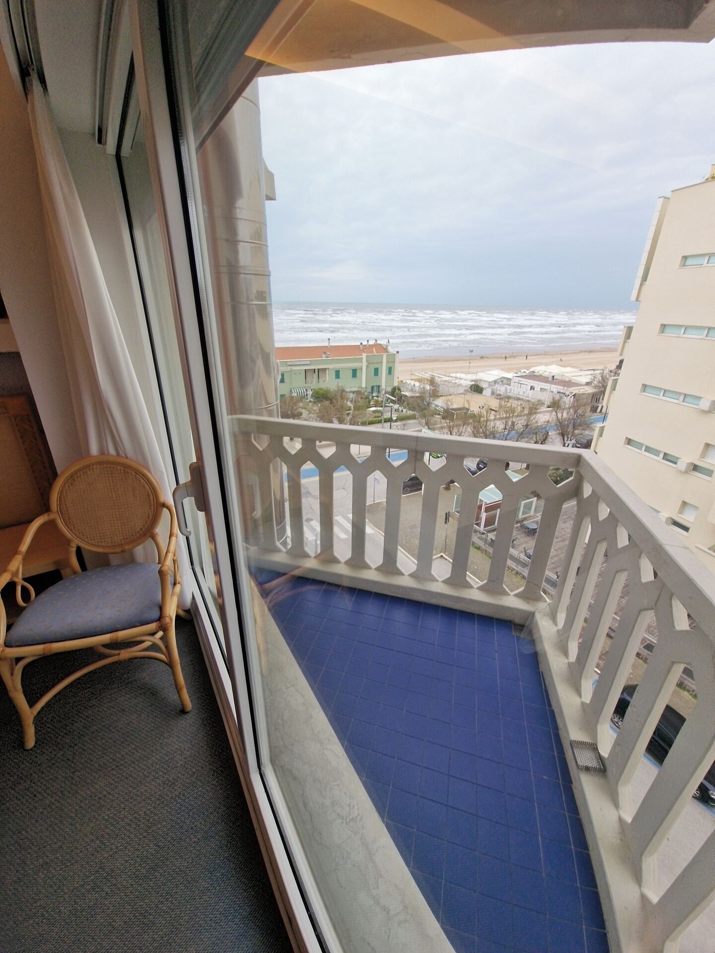 A balcony with a view of the beach, a wicker chair, and a blue floor.