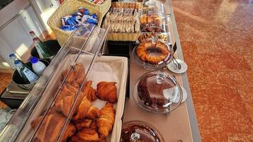 Ein reichhaltiges Buffet mit verschiedenen Speisen, darunter Gebäck und Desserts, sowie eine Theke mit Flaschen und Körben.