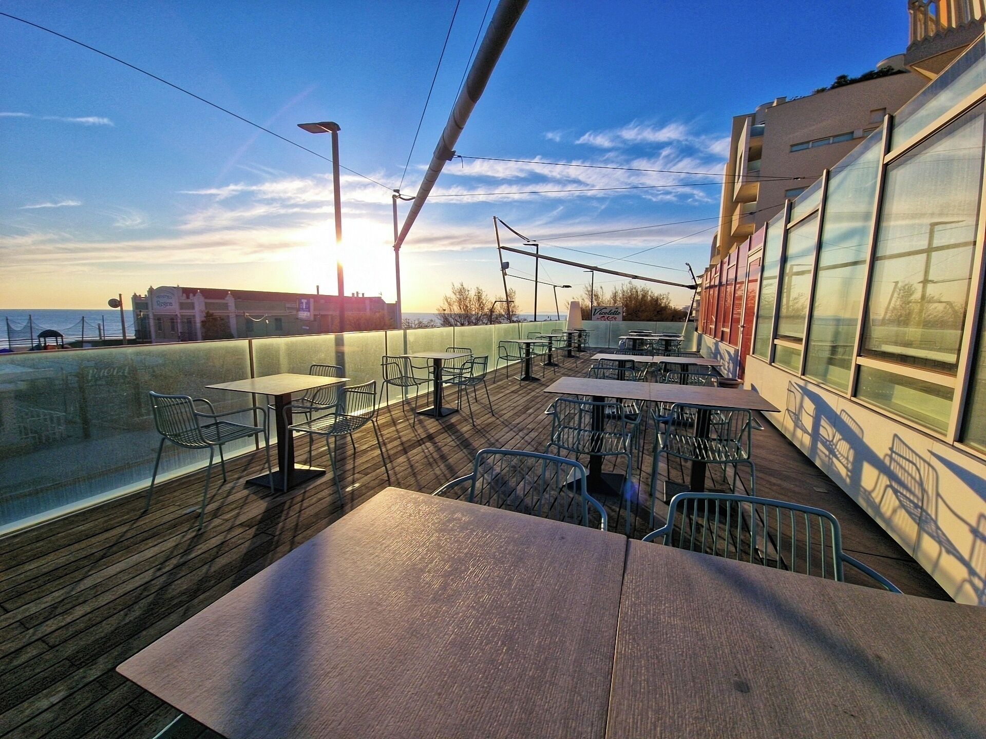 A deck with tables and chairs, overlooking a body of water and buildings.