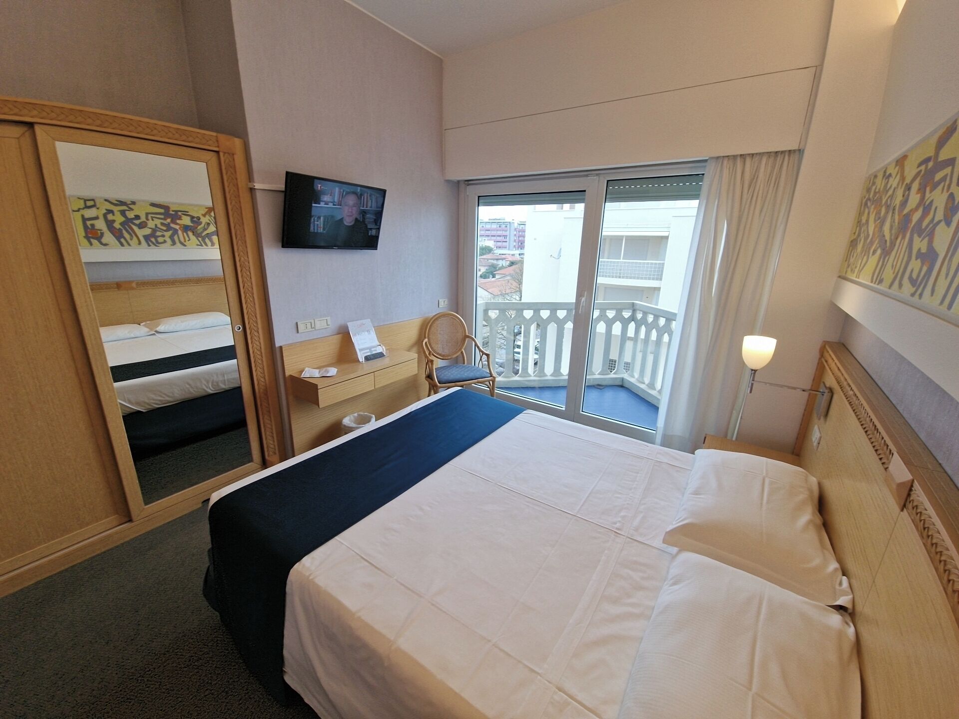 A hotel room with a bed, a desk, a chair, a television, and a balcony with a view.
