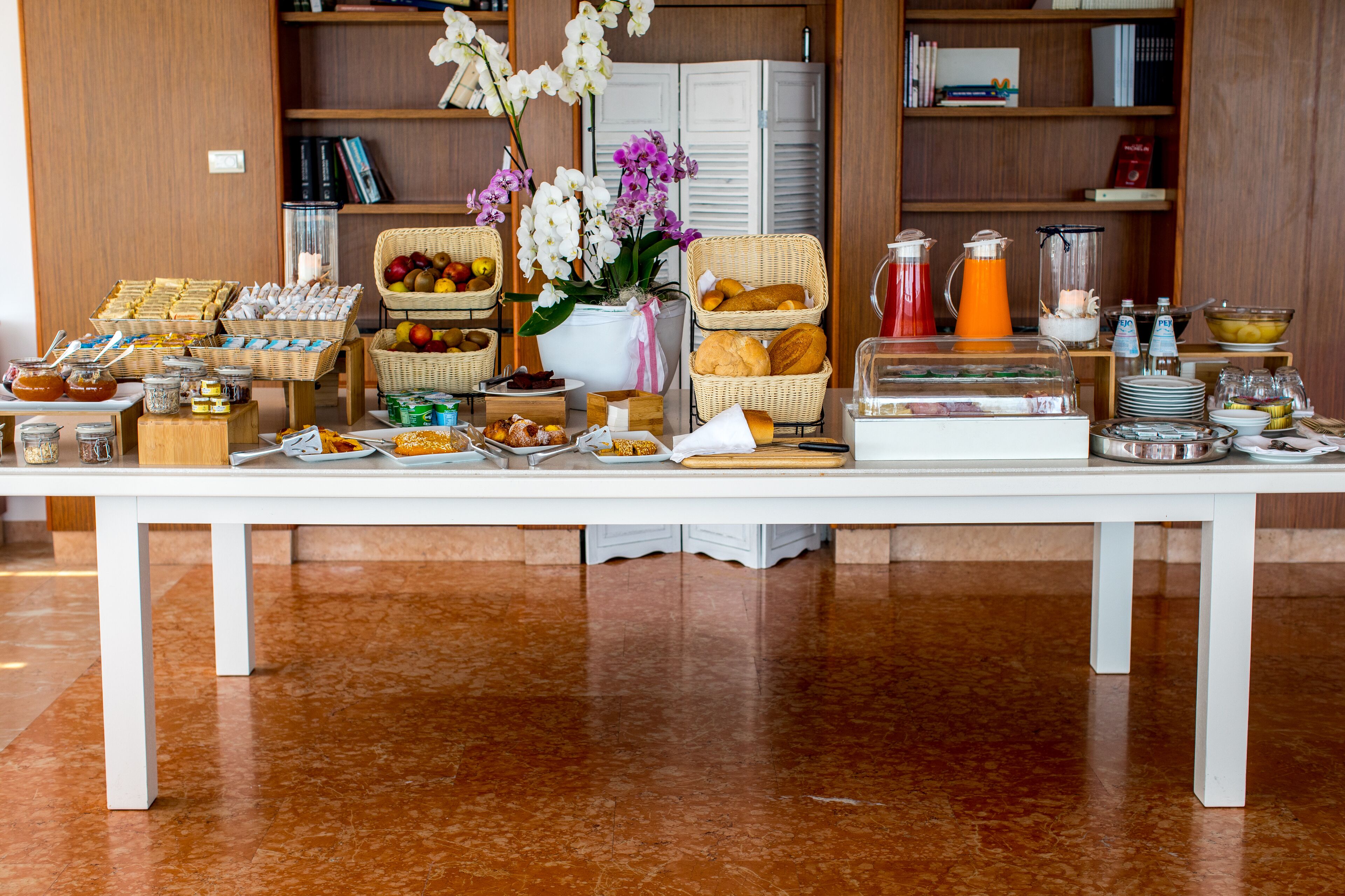 Un bufé de desayuno con diversas opciones de comida y bebidas, como pan, bollería, frutas y una estación de café.