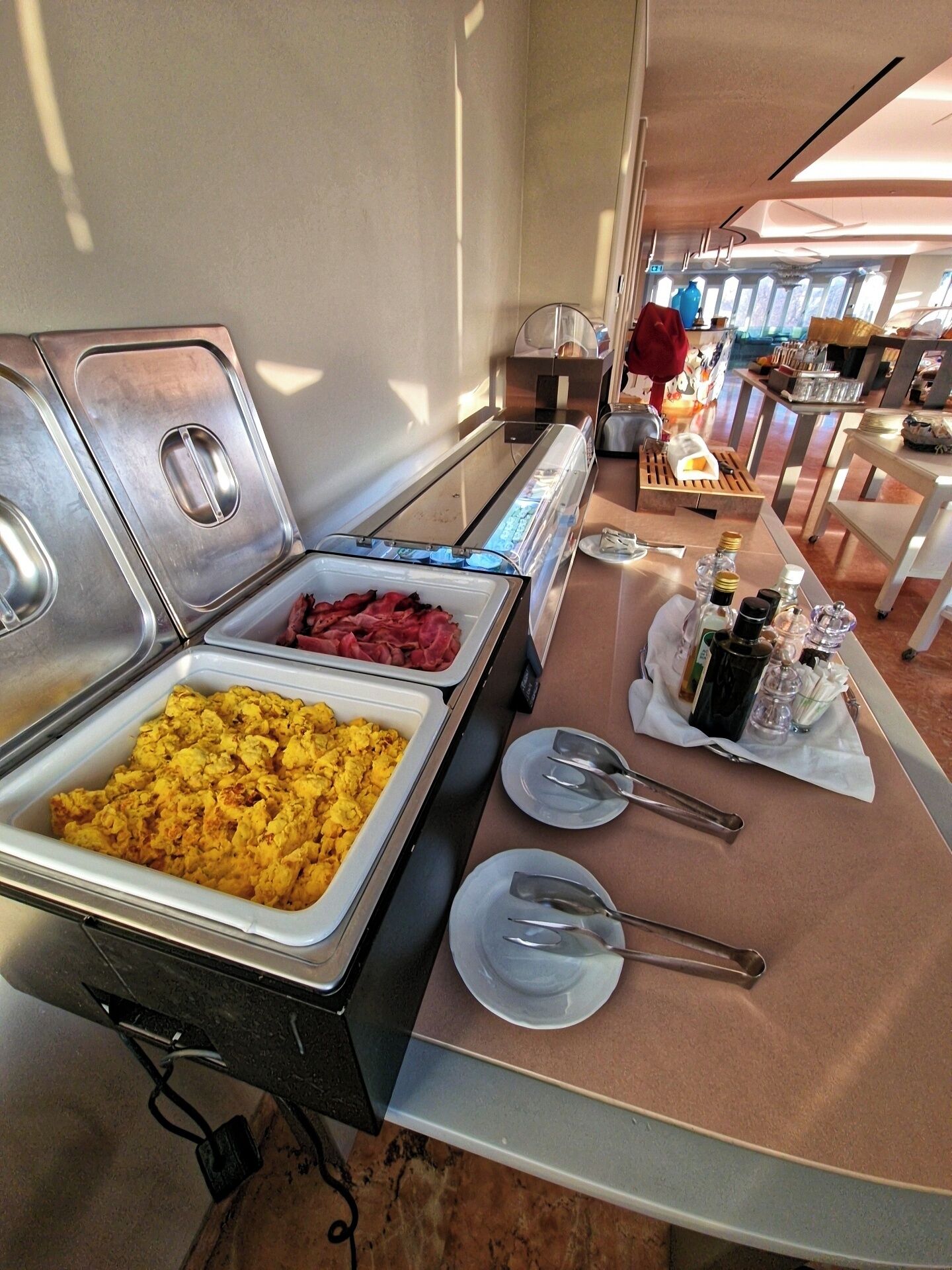A buffet setup with various food items, including scrambled eggs and red meat, and condiments on a table.