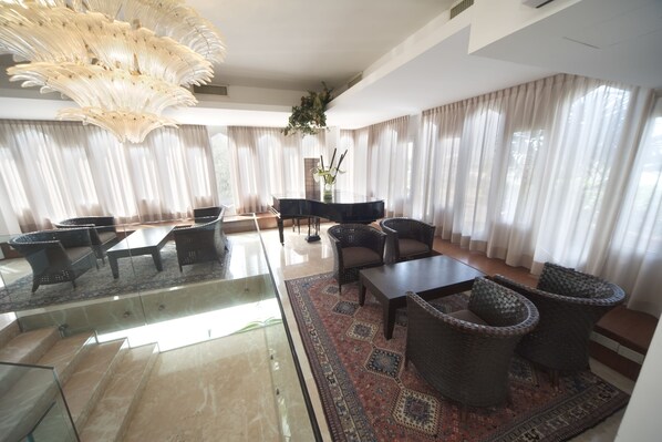 A spacious living room with a piano, comfortable seating, and a large chandelier. - City Hotel (Senigallia)