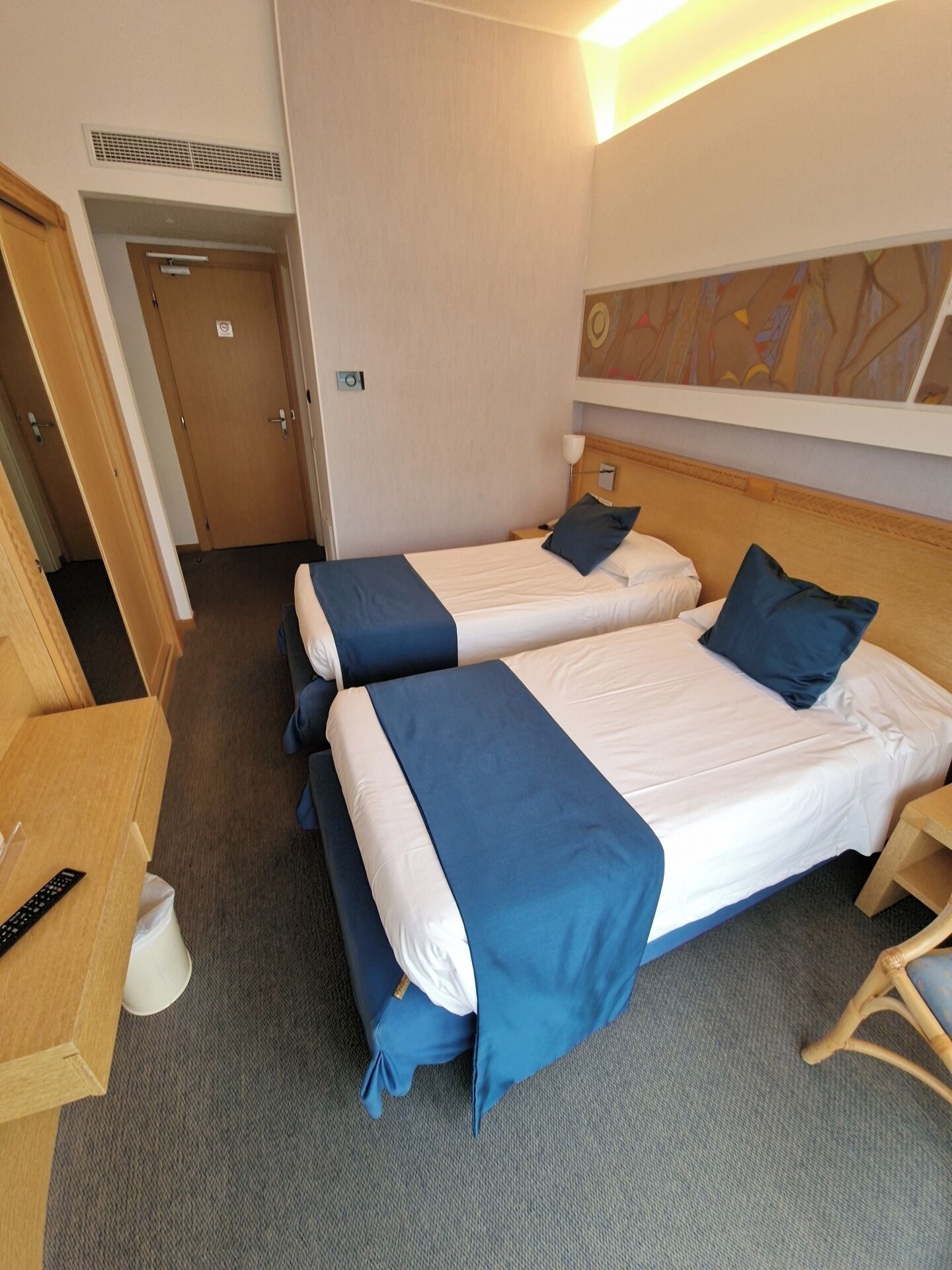 Una habitación de hotel con dos camas, un escritorio, una silla y un cuadro en la pared.