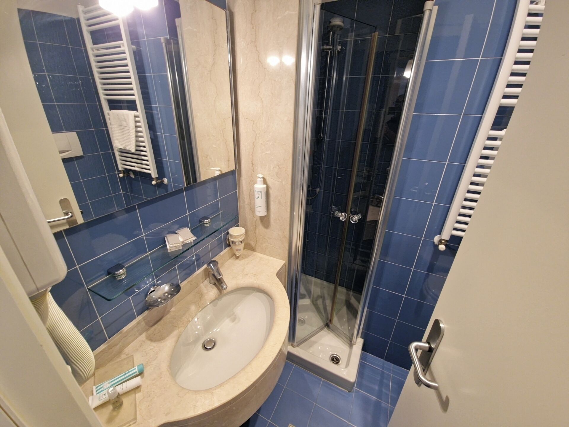 Un baño con lavamanos, espejo, cabina de ducha de vidrio y paredes cubiertas de azulejos azules.