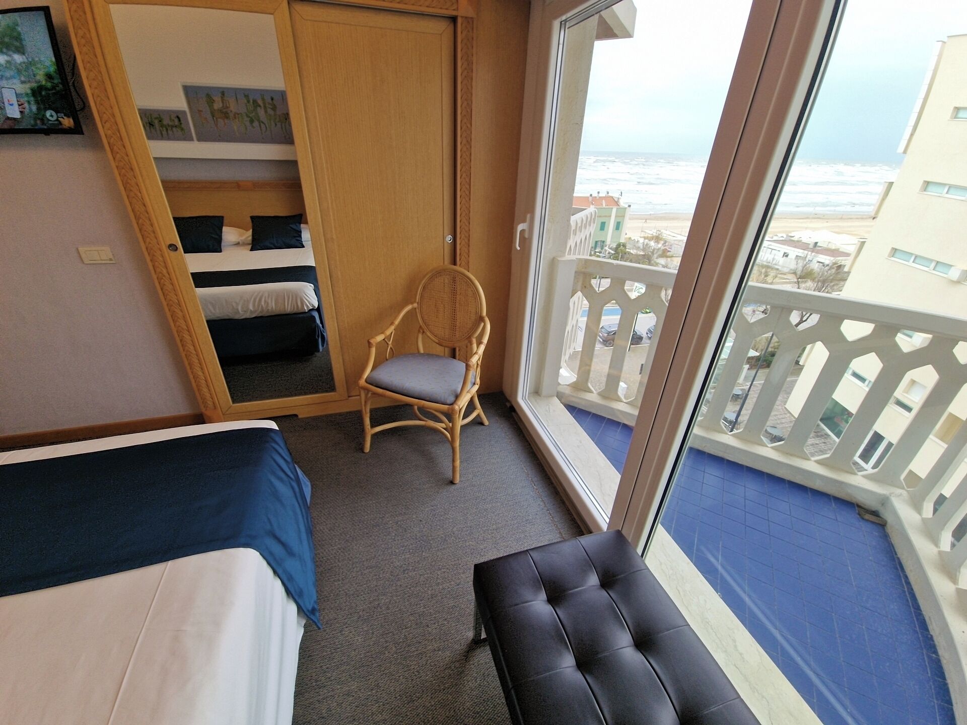 A room with a bed, a chair, a balcony with a railing, and a view of the ocean.