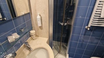 Un baño con ducha envuelta en vidrio, lavamanos con espejo y retrete.