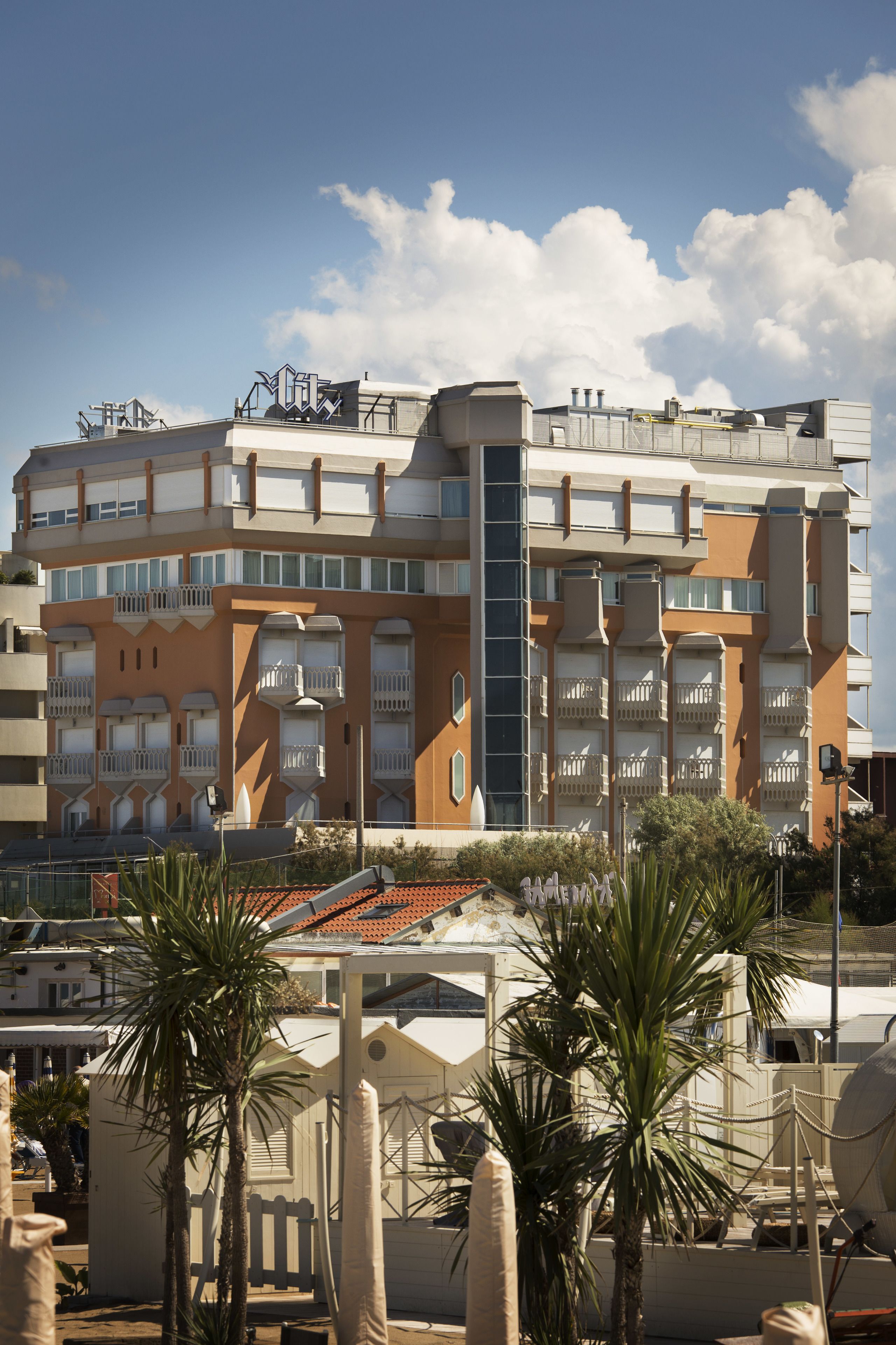 A multi-story building with balconies, a central vertical structure, and a tiled roof.