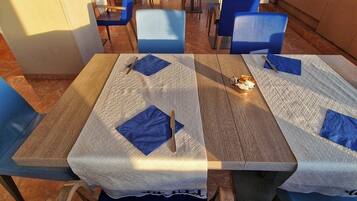 A restaurant with tables covered with white tablecloths and blue napkins, blue chairs, and a view of the outdoors through large windows.