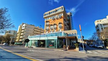 A modern hotel with a glass facade, multiple balconies, and a pedestrian walkway.