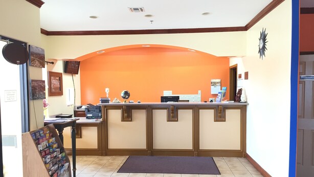 Une salle d’attente avec un bureau, un ordinateur et un globe terrestre. On y trouve une vitrine en bois contenant des livres et un tapis sur le sol.