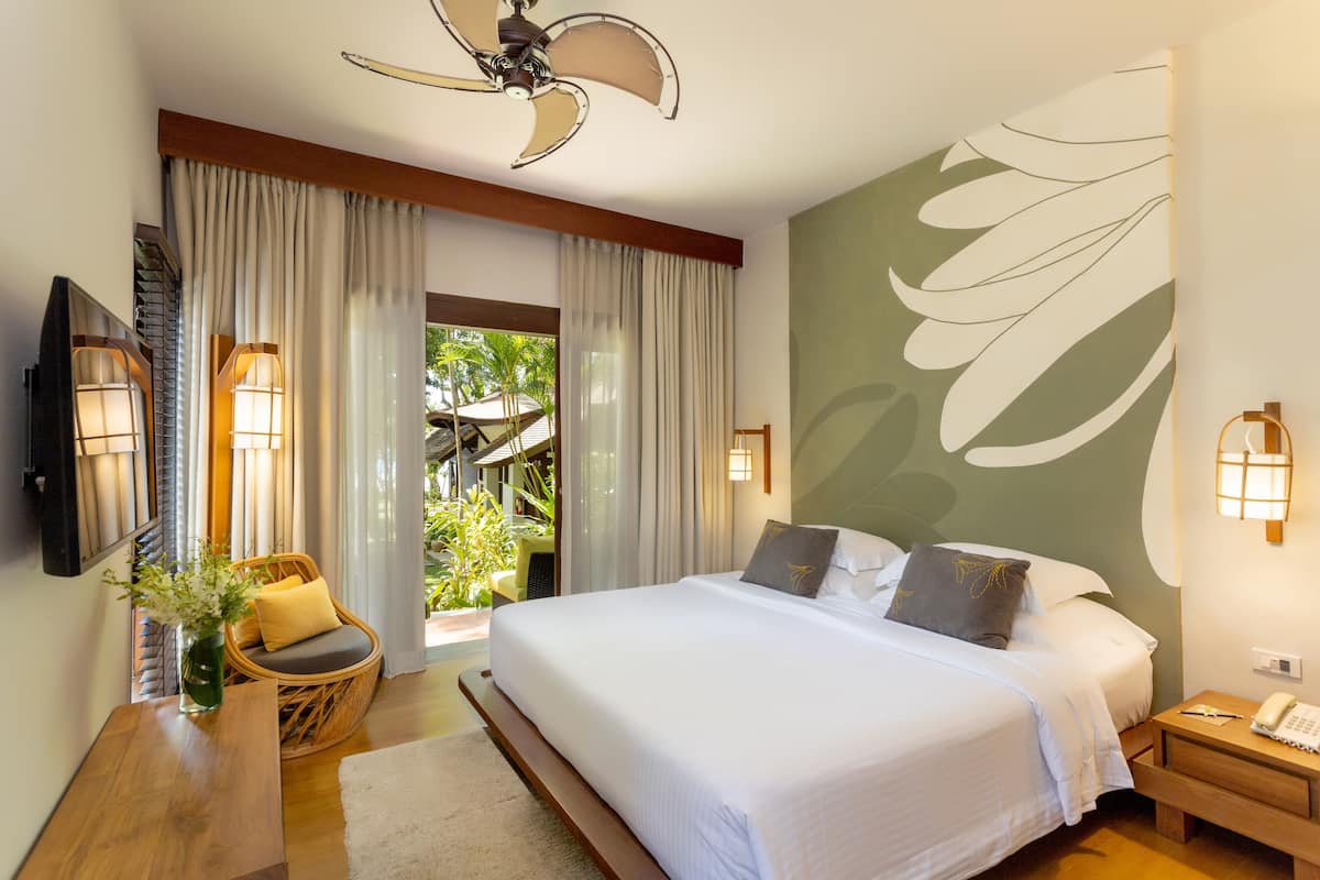 A well-lit bedroom with a large bed, a ceiling fan, a nightstand with a phone, and a view of the outdoors.