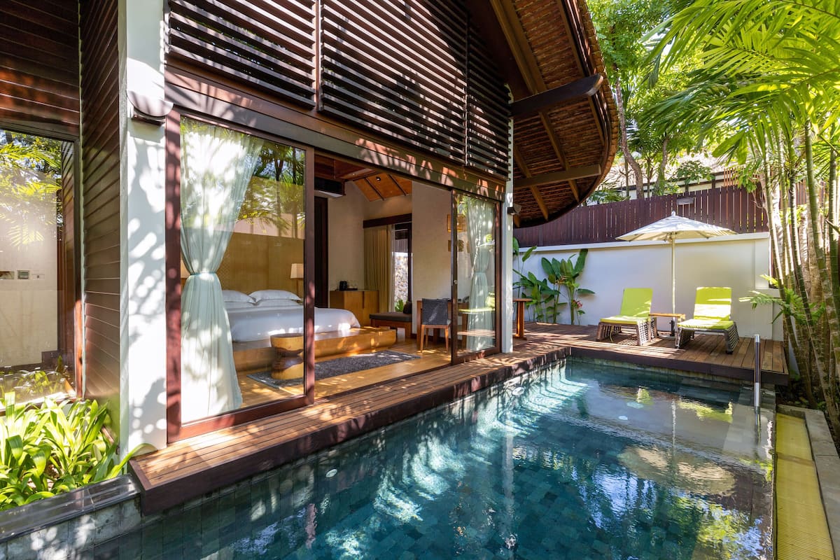 A modern pool area with a wooden deck, a glass-enclosed bedroom, and outdoor seating.