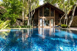 Una piscina con una casa in legno sullo sfondo, circondata da vegetazione lussureggiante.