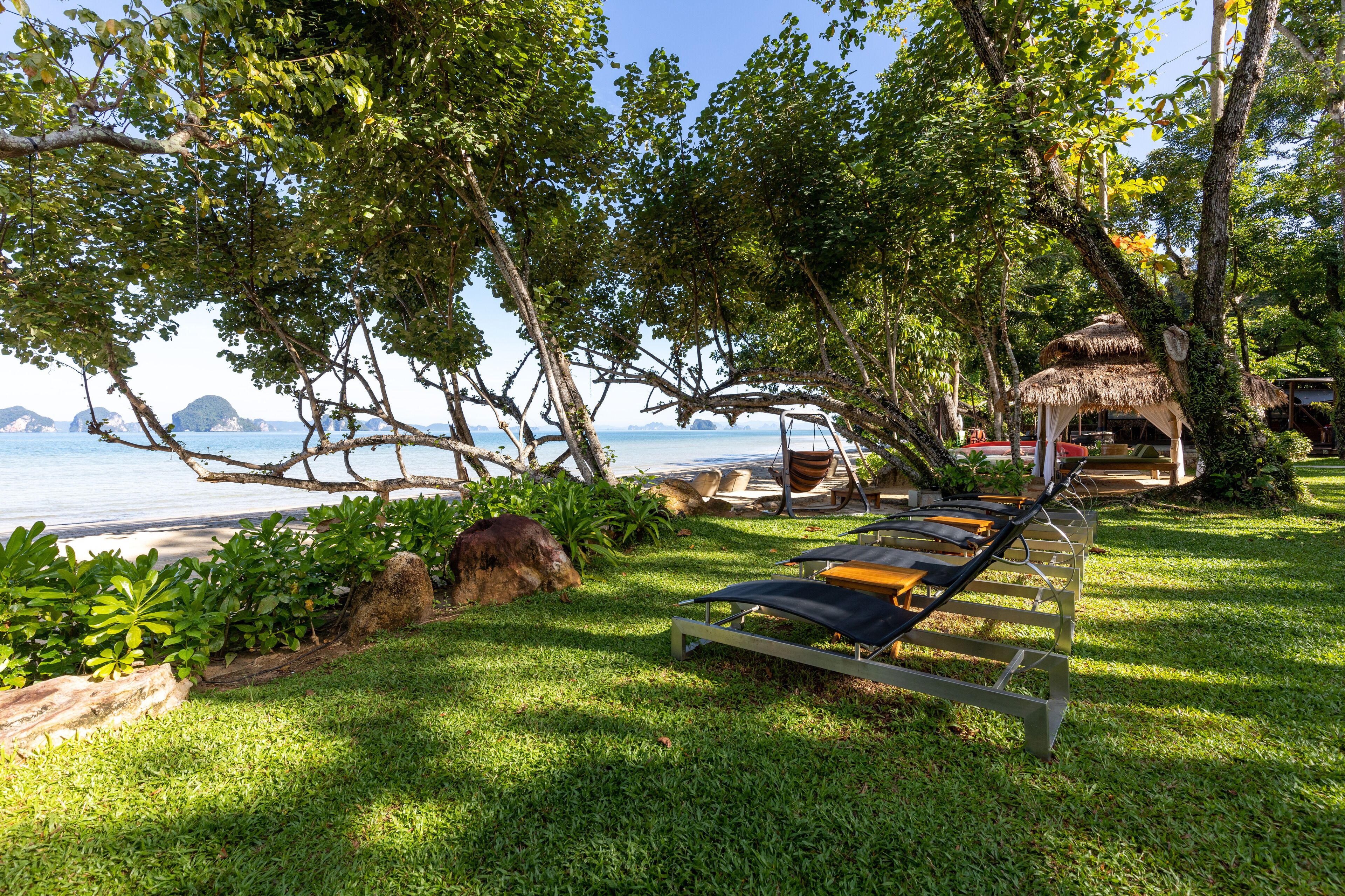 A beachside lounge area with sun loungers, a thatched-roof hut, and a view of the sea and distant islands.