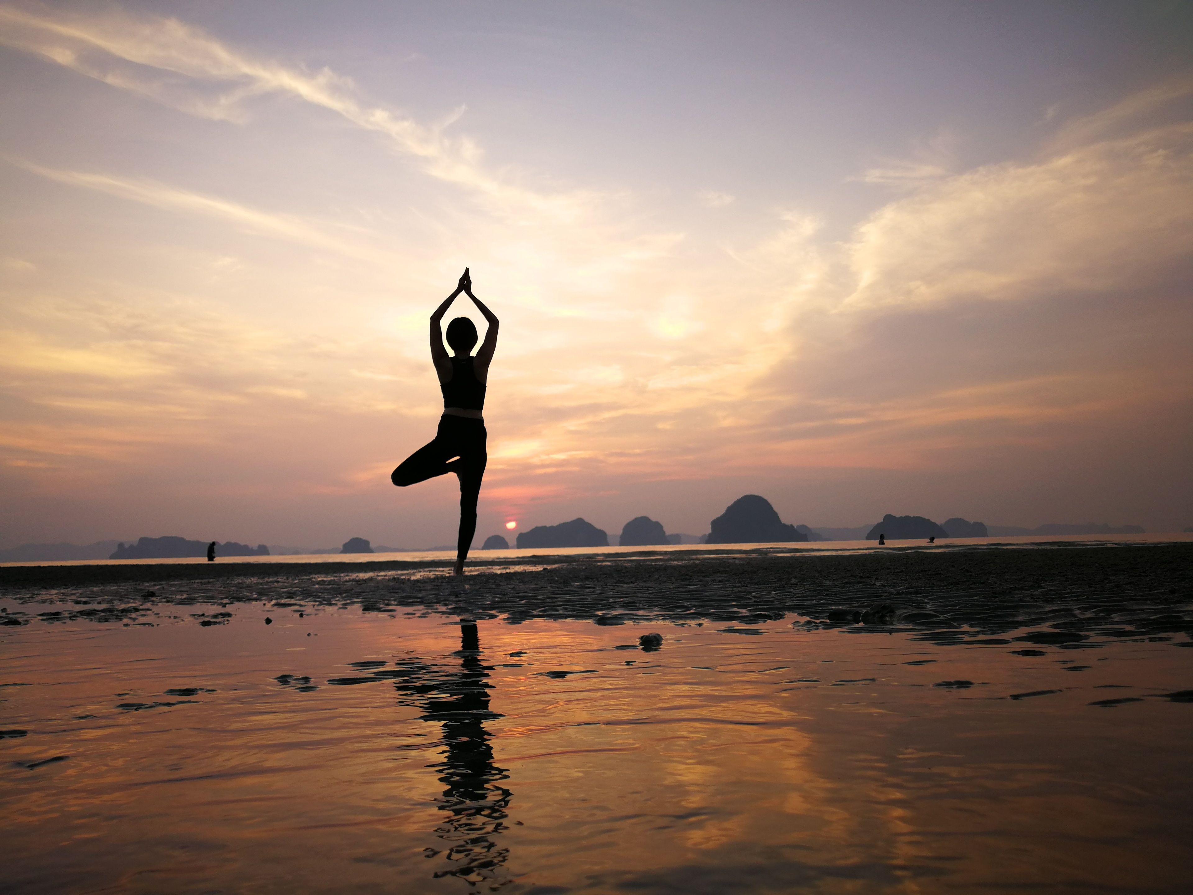 A person performing a yoga pose on a beach at sunset.