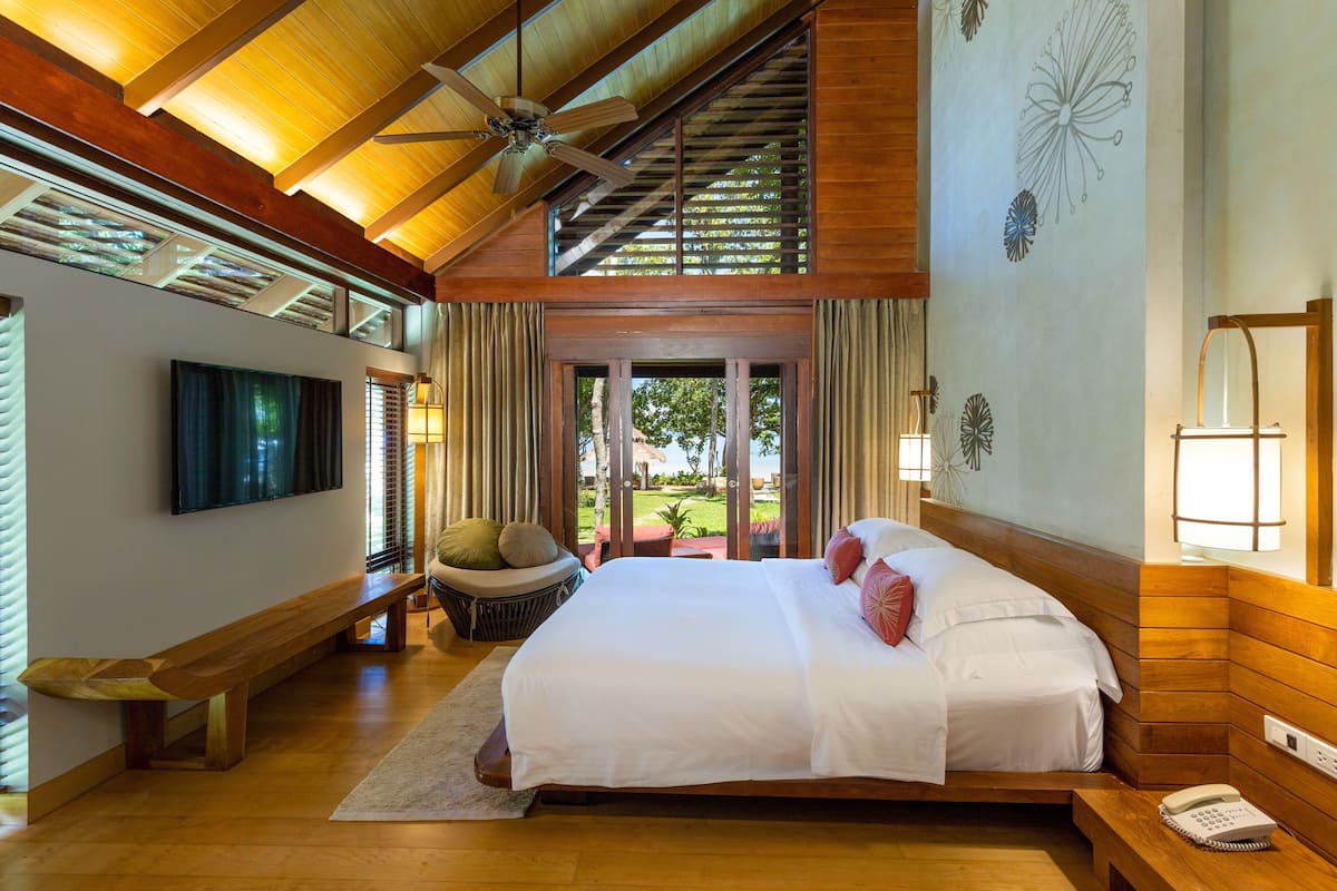 A spacious bedroom with a large bed, wooden ceiling, and a view of the outdoors.