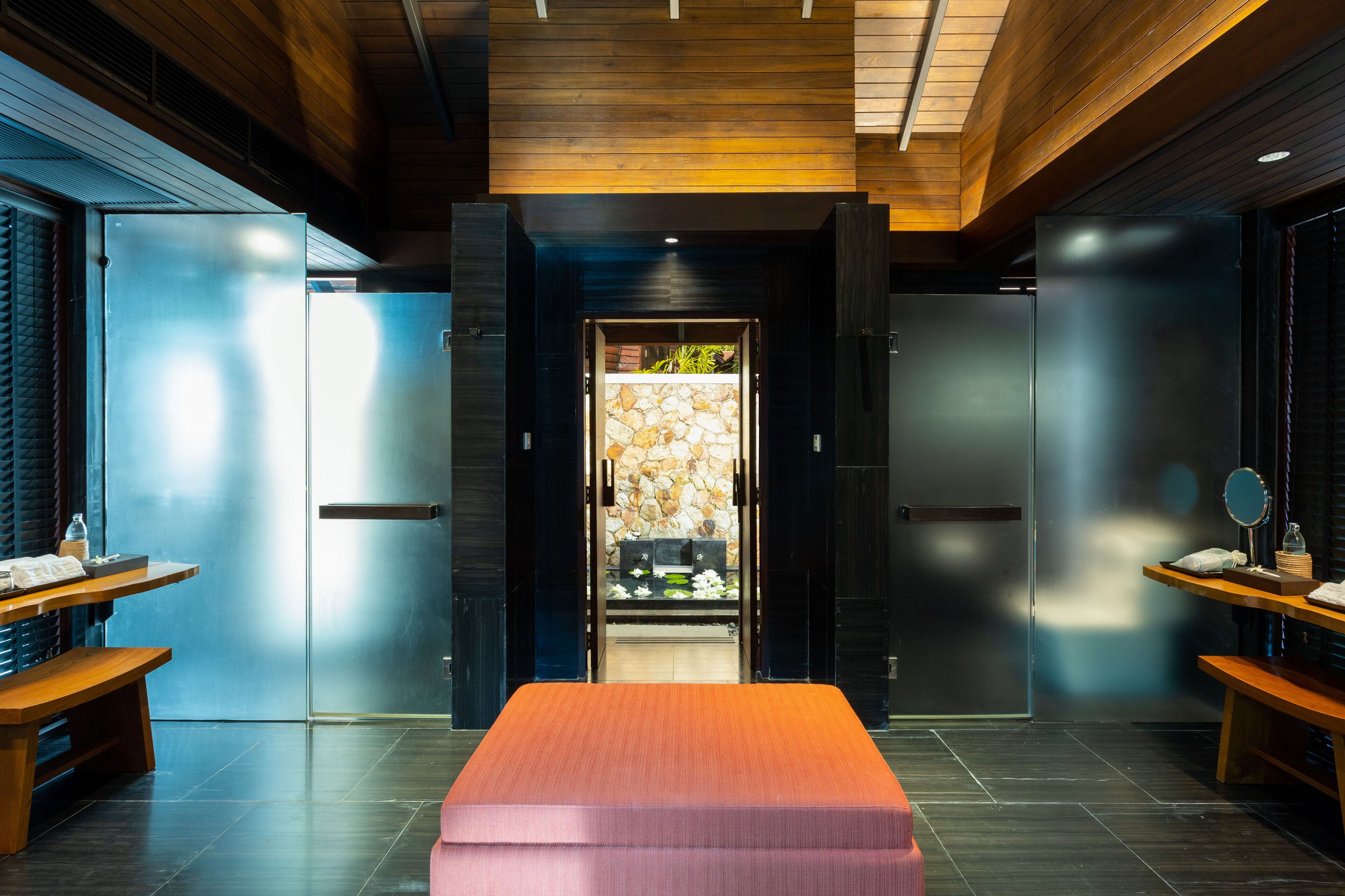 A modern hotel room with a wooden ceiling, a central bench, and a stone wall at the entrance.