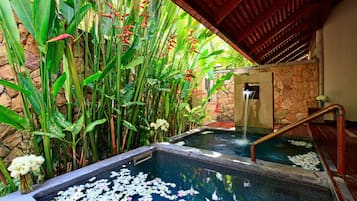 Relax by the serene pool surrounded by lush tropical plants and a stone wall.