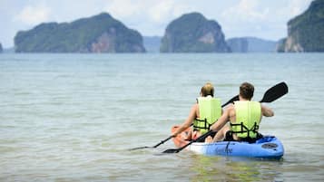 Dos personas hacen kayak en aguas tranquilas, con islas verdes al fondo.