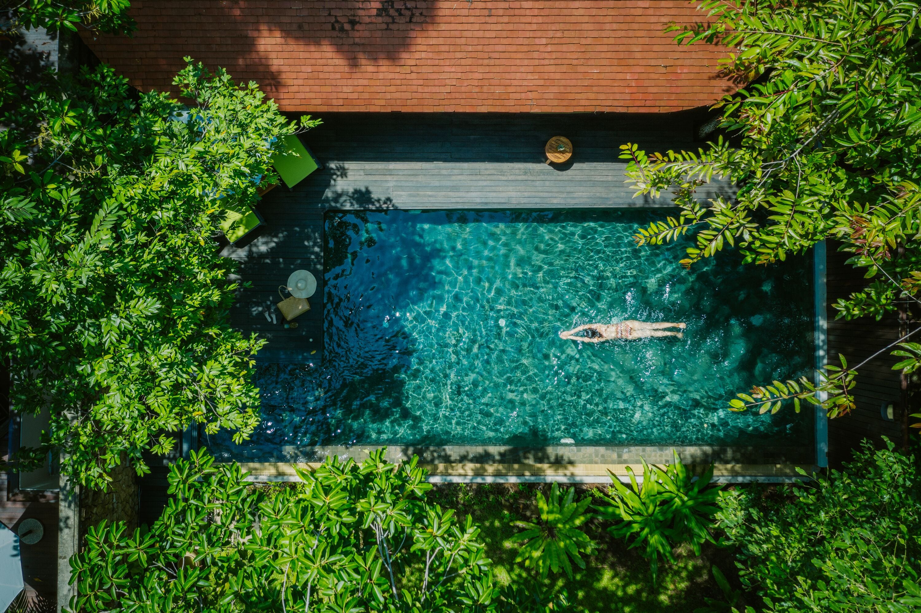 An aerial view of a rectangular swimming pool surrounded by lush greenery, with a person swimming.