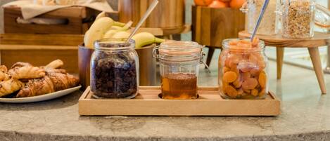 A breakfast buffet with pastries, fruits, and jars of preserves on a marble countertop.