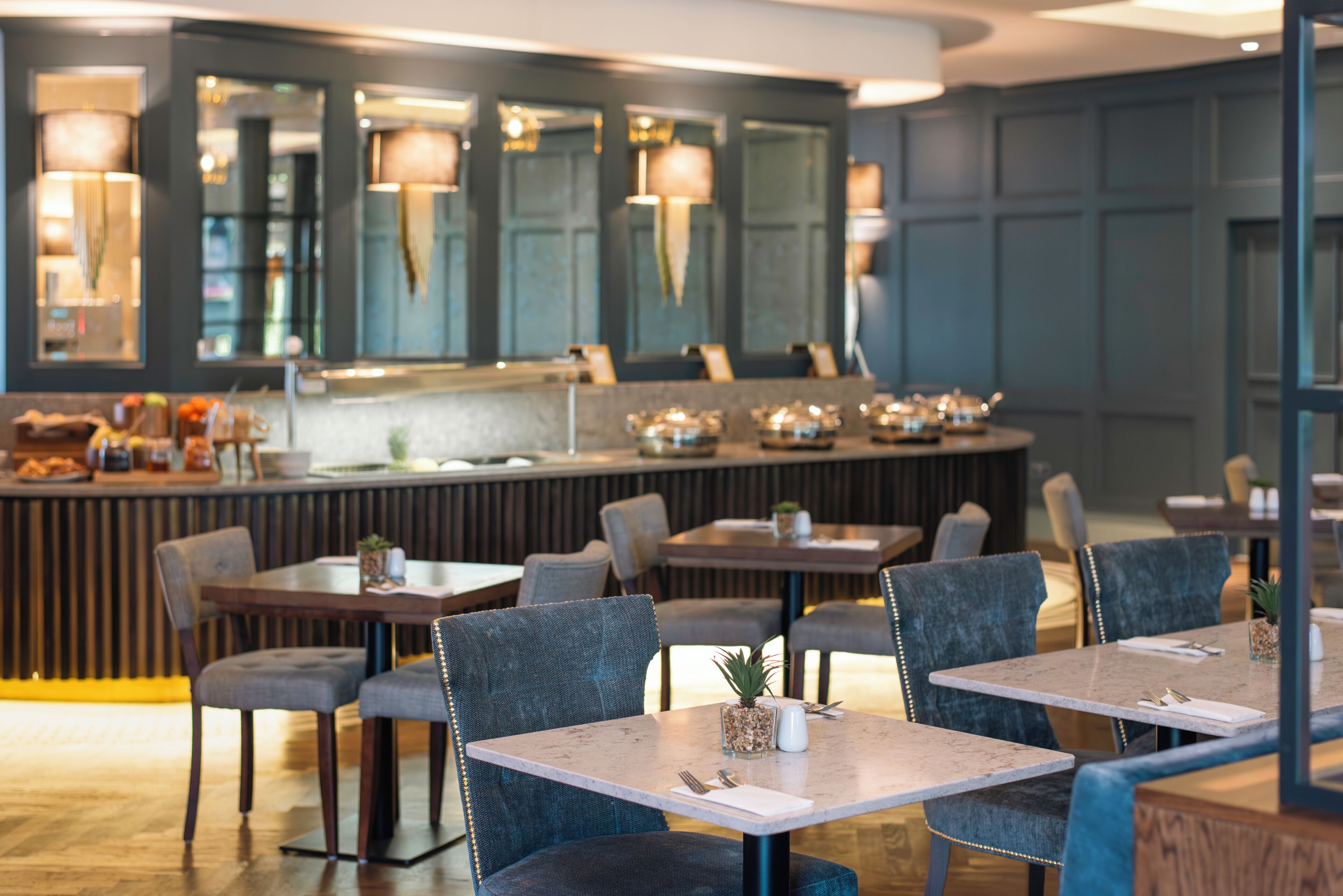 A restaurant with tables and chairs, a counter with food items, and hanging lamps.