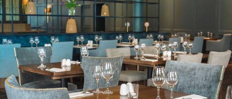Un restaurante con mesas dispuestas para comer, sillas y copas de vino.