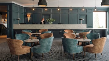 A hotel lobby with teal walls, a marble reception desk, and multiple seating areas with round tables and chairs.