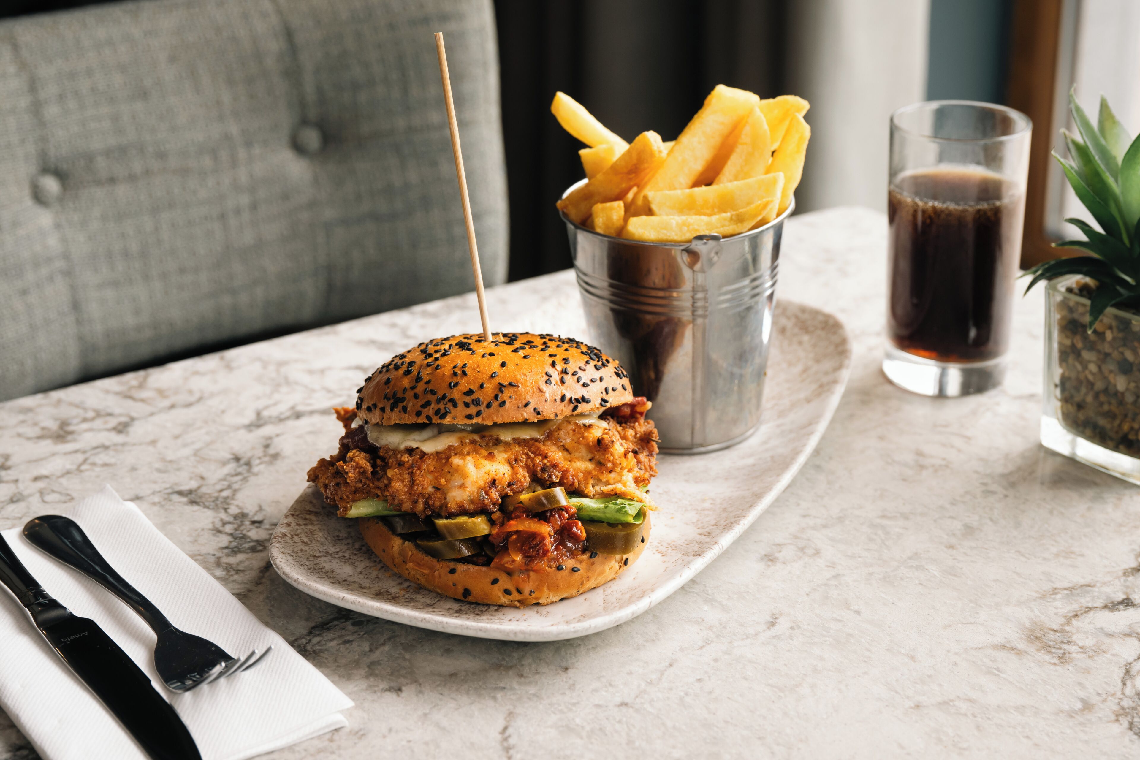 Un hamburger accompagné de frites et d’une boisson, servis sur une table en marbre.