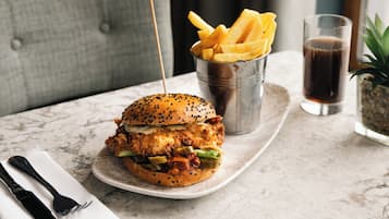 Un hamburger accompagné de frites et d’une boisson, servis sur une table en marbre.