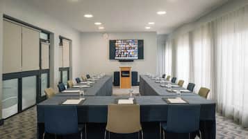 Un salón de conferencias con una larga mesa, sillas, una pantalla y un atril.